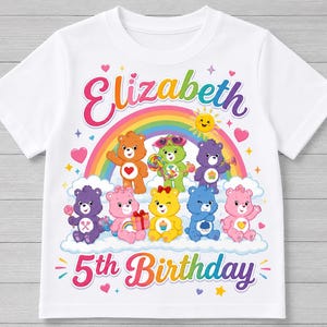 Peut inclure: T-shirt blanc avec un motif coloré représentant le nom "Elizabeth" au-dessus d'un arc-en-ciel et des ours en peluche. Le texte "5th Birthday" est en dessous. Le motif comprend des cœurs, des étoiles et un soleil souriant.