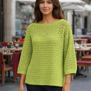 Puede incluir: Un suéter de crochet verde claro, con tejido abierto, cuello barco y mangas tres cuartos. El suéter tiene un aspecto texturizado y un ajuste holgado. Las mangas terminan justo debajo del codo. La prenda está hecha de un material suave y transpirable.
