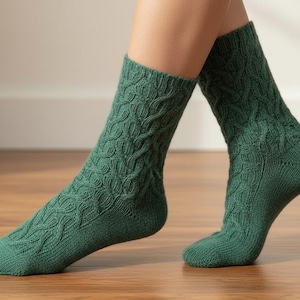 May include: A pair of green knitted socks with a cable knit design. The socks are a solid, deep green colour and appear to be made of a soft, warm material. The socks are on a wooden surface.