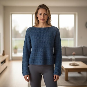Peut inclure: Une personne porte un pull bleu à manches longues avec un col bateau. Le pull présente un motif rayé horizontal texturé. Elle porte également un legging gris. L'arrière-plan montre un salon avec un canapé, une table basse et une grande fenêtre.