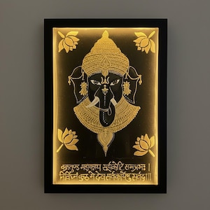 May include: A framed, illuminated artwork featuring a detailed depiction of the Hindu deity Ganesha. The image showcases a black background with a gold-colored Ganesha figure, adorned with intricate details. Four gold lotus flowers surround the central figure, and text is visible at the bottom.
