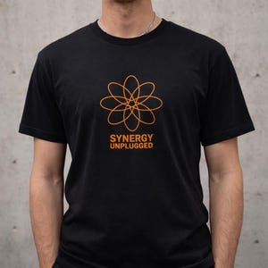 May include: Black t-shirt featuring an orange floral design and the words "SYNERGY UNPLUGGED". The crew neck tee has short sleeves. The graphic is a stylized flower. The shirt is made of a soft material.