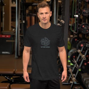 May include: Dark grey t-shirt featuring a geometric pattern and the words "PATTERN LOCKED" in white. The short-sleeved shirt has a crew neck. The design is made of interconnected lines forming a shape.