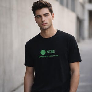 Könnte beinhalten: Schwarzes T-Shirt mit Rundhalsausschnitt und dem grünen Text "MINE OWNERSHIP NULLIFIED". Das Design beinhaltet einen grünen Kreis über dem Wort "MINE". Das Shirt ist aus weichem Material.