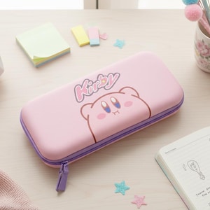 May include: A pink pencil case featuring the character Kirby with the word "Kirby" above the character's face. The case has a purple zipper and trim. The case is on a light wood surface with a succulent, sticky notes, and a floral mug.