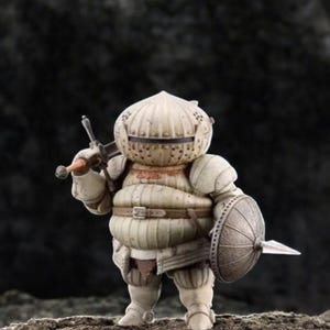 May include: A detailed figurine of a knight in off-white armor, holding a sword and shield. The knight has a round helmet and a stout build, with a belt around the waist. The shield has a spear attached. The figurine is on a textured surface.