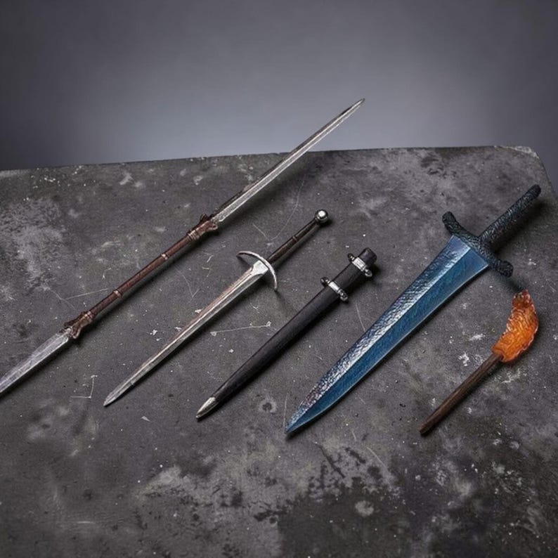 May include: A collection of four items including a long thin spear with a metallic tip, a slender silver-toned dagger, a black-sheathed dagger with silver accents, and a blue-bladed short sword next to a small amber-colored pointed object.