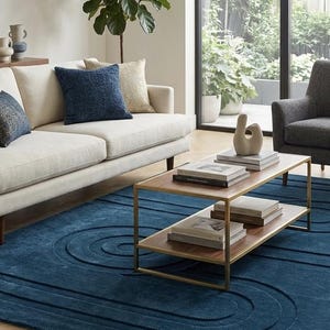 May include: A large rectangular area rug in a deep blue hue featuring a raised, carved geometric pattern of concentric rounded lines. The rug is positioned on a light-coloured wooden floor, providing a textured foundation for the living room furniture.