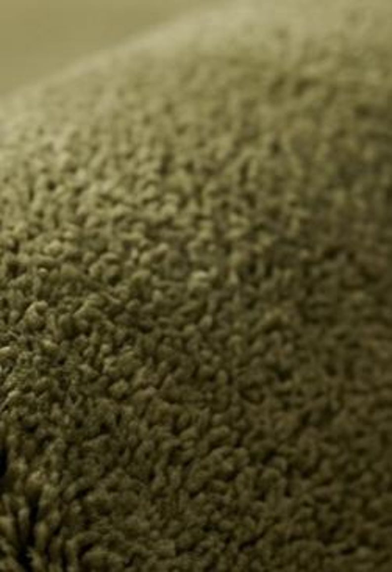 May include: A close-up view of a textured olive green fabric with a dense, looped pile surface. The material features a consistent, soft, and fuzzy appearance with small, uniform loops creating a tactile, uneven surface across the entire frame.
