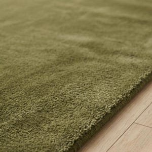 May include: A solid olive green area rug with a thick, plush, and textured pile surface. The rug features a dense, soft-touch fabric construction with a consistent monochromatic color throughout, showcasing a deep, earthy green tone and a soft finish.