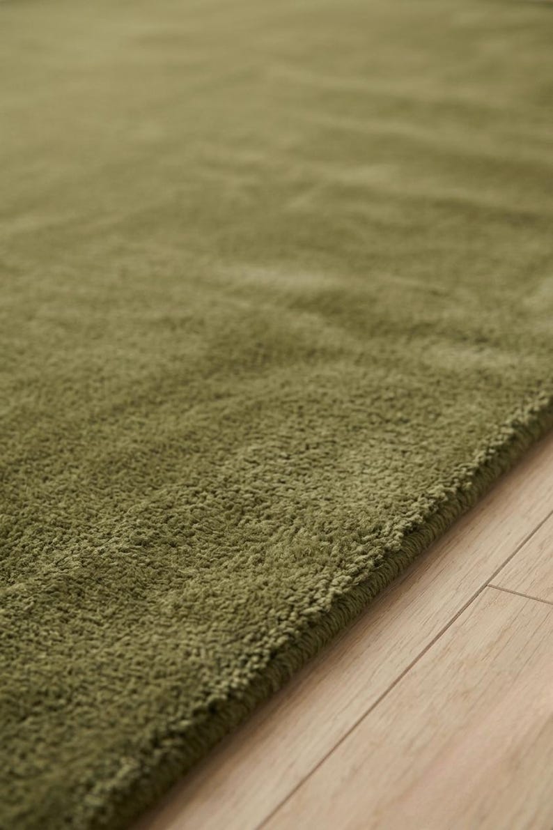 May include: A solid olive green area rug with a thick, plush, and textured pile surface. The rug features a dense, soft-touch fabric construction with a consistent monochromatic color throughout, showcasing a deep, earthy green tone and a soft finish.