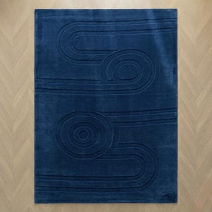 K&ouml;nnte beinhalten: Ein rechteckiger Teppich in tiefem Marineblau mit einem erhabenen, geschnitzten Muster aus konzentrischen Kreisen und geschwungenen, parallelen Linien, die ein strukturiertes, geometrisches Design auf der gesamten Oberfl&auml;che bilden.
