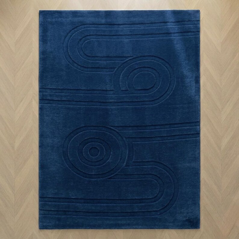 K&ouml;nnte beinhalten: Ein rechteckiger Teppich in tiefem Marineblau mit einem erhabenen, geschnitzten Muster aus konzentrischen Kreisen und geschwungenen, parallelen Linien, die ein strukturiertes, geometrisches Design auf der gesamten Oberfl&auml;che bilden.