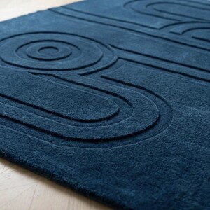 K&ouml;nnte beinhalten: Ein tief dunkelblauer Teppich mit einer erhabenen, geschnitzten Textur, die eine Reihe konzentrischer Kreise und l&auml;nglicher, abgerundeter geometrischer Linien auf der Oberfl&auml;che bildet und ein haptisches, dreidimensionales Muster erzeugt.