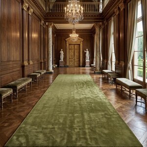 May include: A long, rectangular olive green area rug with a soft, plush texture centered on a polished dark wood parquet floor. The rug spans the length of a grand hallway featuring wood-paneled walls, marble columns, and crystal chandeliers.