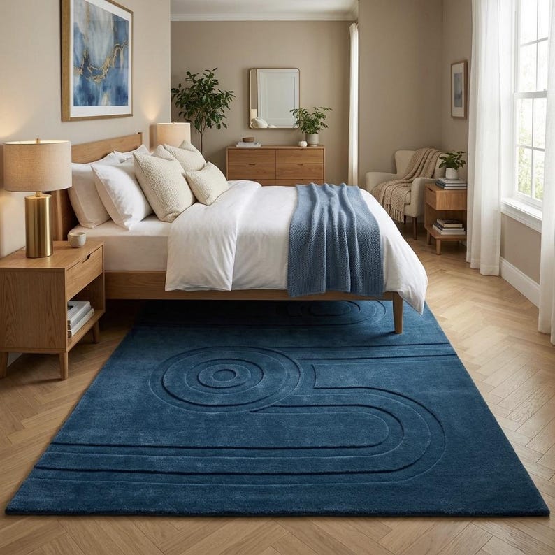 K&ouml;nnte beinhalten: Ein rechteckiger Teppich in tiefem Marineblau mit einem erhabenen, strukturierten Muster aus konzentrischen Kreisen und parallelen Linien. Der Teppich liegt auf einem hellen Fischgr&auml;t-Holzboden in einem Schlafzimmer mit Bett und M&ouml;beln.
