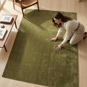 May include: A rectangular area rug in a solid olive green color with a short, dense pile texture. The rug is laid flat on a light-colored wooden floor, showcasing a uniform surface and clean, straight edges throughout its entire perimeter.