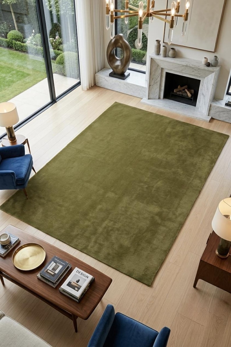 May include: A large, rectangular area rug in a solid olive green color with a smooth, low-pile texture. The rug is positioned centrally on a light-colored wooden floor, covering a significant portion of the floor space in the room.