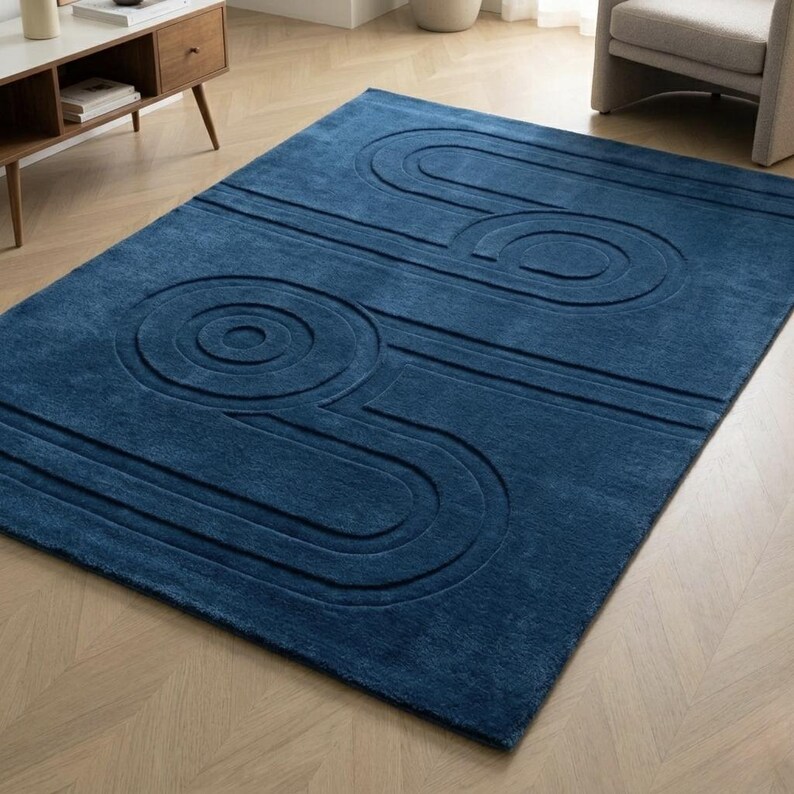 K&ouml;nnte beinhalten: Ein rechteckiger Teppich in tiefem Marineblau mit einer erhabenen, geschnitzten Textur, die ein Muster aus konzentrischen Kreisen und parallelen Linien auf der Oberfl&auml;che bildet. Der Teppich hat einen weichen Flor und einen einheitlichen Blauton.