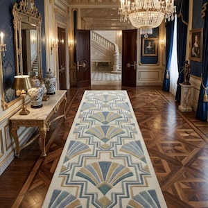 Puede incluir: Una alfombra rectangular con un diseño geométrico de abanico en tonos azules, beige y grises. La alfombra está colocada sobre un suelo de madera oscura en un gran pasillo con molduras doradas, paredes azules y una lámpara de araña.