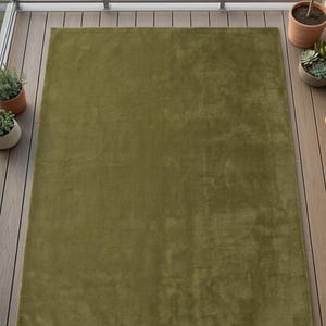 May include: A rectangular area rug in a solid olive green color with a soft, plush texture. The rug features a uniform, monochromatic surface with a short pile finish, providing a consistent appearance across the entire rectangular shape.