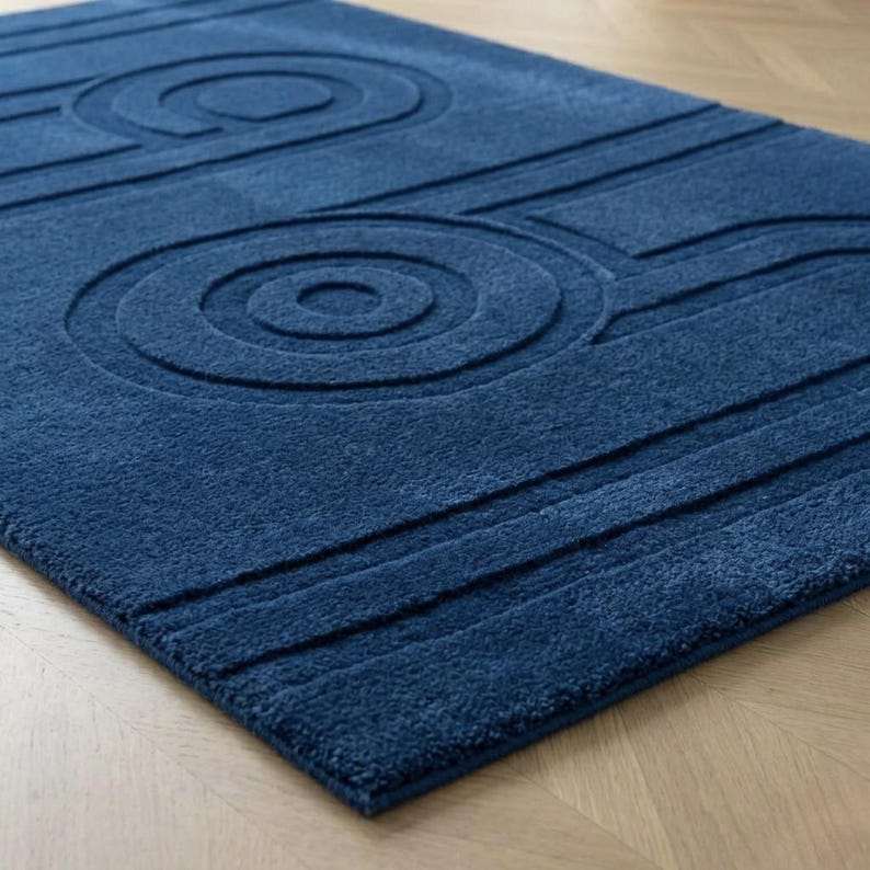 K&ouml;nnte beinhalten: Ein rechteckiger, tiefblauer Teppich mit einem erhabenen, strukturierten Muster aus konzentrischen Kreisen und parallelen Linien. Der Teppich hat eine dicke, flauschige Oberfl&auml;che mit einer durchgehend einheitlichen Farbe.