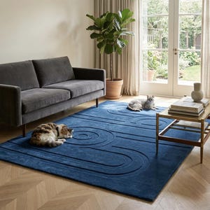 K&ouml;nnte beinhalten: Ein rechteckiger Teppich in tiefem Marineblau mit einem erhabenen, geschnitzten geometrischen Muster aus konzentrischen Kreisen und l&auml;nglichen ovalen Linien. Der Teppich liegt auf einem hellen Holzboden mit Fischgr&auml;tenmuster.