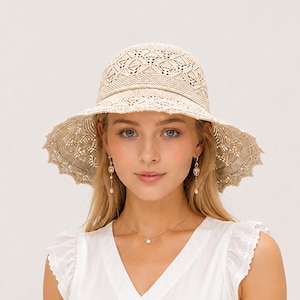 May include: A beige crochet sun hat featuring an intricate diamond pattern on the crown and a wide, scalloped brim. The hat is constructed from a textured, woven material with a matching thin cord detail encircling the base of the crown.