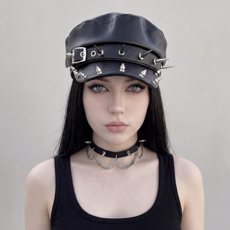 Puede incluir: Gorra de cuero negra con p&uacute;as plateadas y una hebilla. Tambi&eacute;n se ve un collar gargantilla negro a juego con cadenas y p&uacute;as plateadas. Los art&iacute;culos son parte de un conjunto de moda g&oacute;tica.