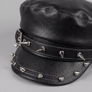 Puede incluir: Gorra de cuero negro con tachuelas c&oacute;nicas plateadas alrededor del borde y la banda. La gorra tiene un dise&ntilde;o estructurado con detalles de costura blanca. Una hebilla plateada asegura la banda.