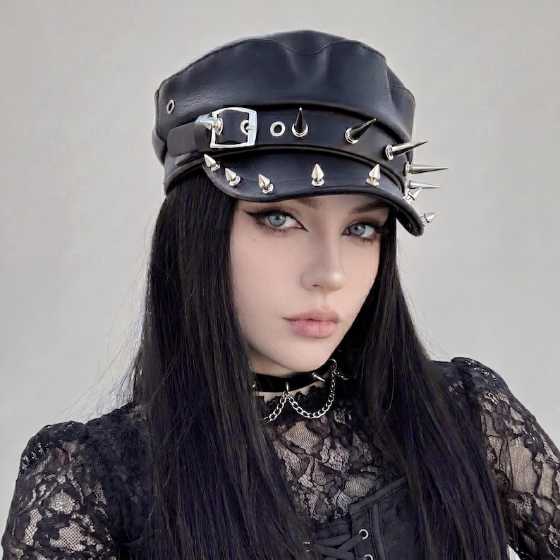 Puede incluir: Gorra de cuero negra con p&uacute;as y tachuelas de metal plateado. La gorra tiene un cierre de hebilla y una peque&ntilde;a visera. Un accesorio elegante para un look atrevido y vanguardista.