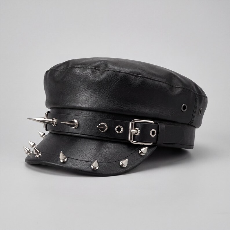 Puede incluir: Gorra negra de cuero sint&eacute;tico con p&uacute;as de metal plateado y cierre de hebilla. El sombrero tiene una parte superior plana y una visera corta, con una correa decorativa. Un accesorio de moda.