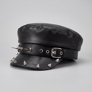 Puede incluir: Gorra negra de cuero sint&eacute;tico con la parte superior plana y una visera corta. El sombrero presenta una hebilla y una correa plateadas, y est&aacute; adornado con p&uacute;as plateadas a lo largo del borde y en la correa. Estilo militar cl&aacute;sico.