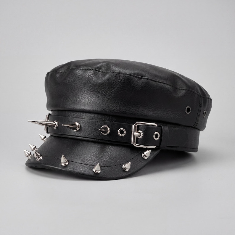 Puede incluir: Gorra negra de cuero sint&eacute;tico con la parte superior plana y una visera corta. El sombrero presenta una hebilla y una correa plateadas, y est&aacute; adornado con p&uacute;as plateadas a lo largo del borde y en la correa. Estilo militar cl&aacute;sico.