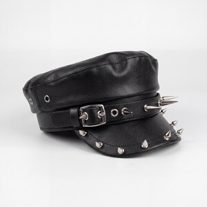 Puede incluir: Gorra negra de cuero sint&eacute;tico con visera corta y correa decorativa. La correa y la visera est&aacute;n adornadas con p&uacute;as y tachuelas plateadas. La gorra presenta un cierre de hebilla y ojales.