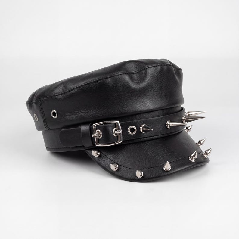 Puede incluir: Gorra negra de cuero sint&eacute;tico con visera corta y correa decorativa. La correa y la visera est&aacute;n adornadas con p&uacute;as y tachuelas plateadas. La gorra presenta un cierre de hebilla y ojales.