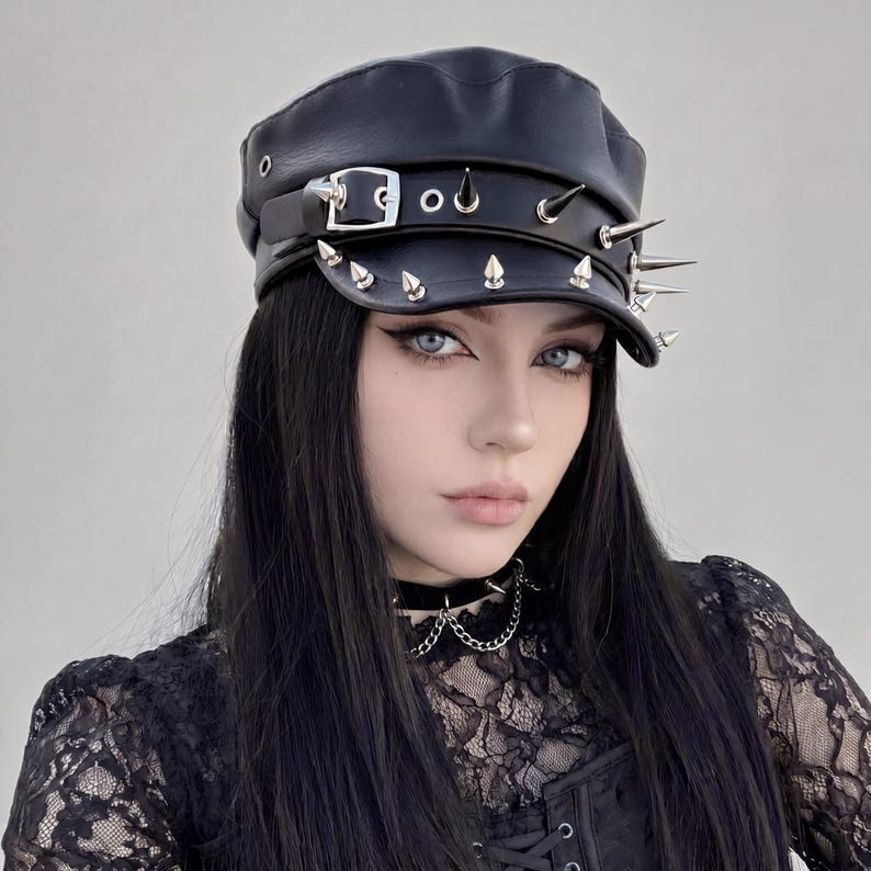 Puede incluir: Gorra de cuero negro con p&uacute;as y hebillas plateadas. La gorra tiene una visera plana y una corona estructurada. El sombrero es un accesorio oscuro, adecuado para la moda alternativa.