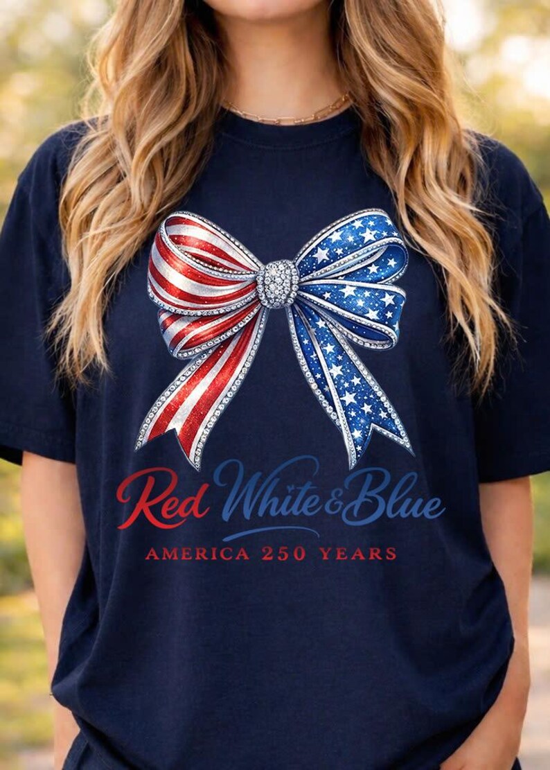 May include: Dark blue t-shirt with a bow design in red, white, and blue, with a star pattern. The text reads "Red White & Blue AMERICA 250 YEARS". A patriotic themed top.