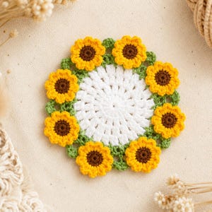Può includere: Sottobicchiere a forma di girasole all'uncinetto. Il centro è bianco, circondato da girasoli gialli con centri marroni e foglie verdi. Un oggetto fatto a mano per l'arredamento della casa.