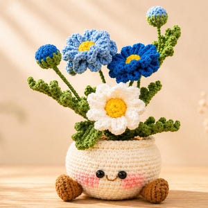 May include: A crocheted flower arrangement in a white pot with a smiling face. The arrangement features blue and white flowers with yellow centers, green leaves, and brown feet. The pot is round and has a cute, friendly design.