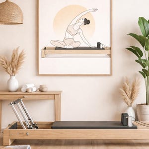 Può includere: Illustrazione incorniciata di una persona che fa Pilates su un reformer. L'opera d'arte è in stile minimalista con una calda tavolozza di colori. Un reformer Pilates è in primo piano, con un tappetino da yoga e altri accessori.