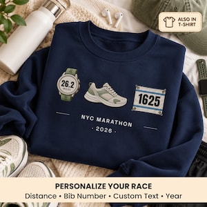 May include: A navy blue crewneck sweatshirt featuring a graphic of a sports watch displaying 26.2 miles, a running shoe, and a race bib with the number 1625. Below the graphics, the text reads NYC MARATHON and 2026 in white lettering.