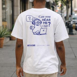 May include: White t-shirt with a blue graphic on the back featuring a chicken wearing headphones and using a laptop. Text on the shirt reads "Can you HEAR ME? Club" and "BUTT IN CHAIR".