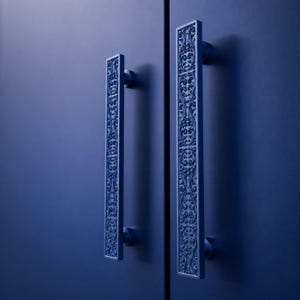 Può includere: Due maniglie per porta rettangolari verticali con una finitura blu opaco profondo. Ogni maniglia presenta un motivo in rilievo floreale e a volute complesso e continuo lungo tutta la sua lunghezza, montata su una porta blu tinta unita.