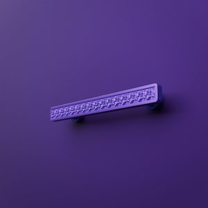 Puede incluir: Un tirador de mueble rectangular con un acabado en color violeta vibrante. El tirador presenta una franja horizontal central con un patrón de superficie texturizado y cristalino, flanqueado por bordes violetas lisos y sólidos en los lados superior e inferior.