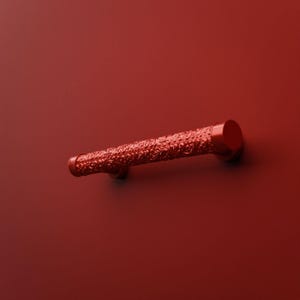 Peut inclure: Une poignée de meuble rouge solide présentant une barre cylindrique avec un motif floral en relief complexe sur toute sa longueur, terminée par des embouts circulaires plats et lisses de chaque côté de la pièce de quincaillerie.