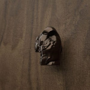 Op de afbeelding: Een donkerbruine, gebeeldhouwde meubelknop in de vorm van een buldogkop. De knop heeft een gladde, glanzende afwerking met gegoten details die de oren, ogen en snuit van de hond definiëren, wat zorgt voor een functionele grip voor deuren.