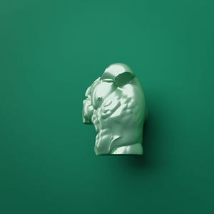 Op de afbeelding: Een metallic lichtgroen beeldhouwwerk van een menselijke torso, met gedefinieerde buik- en borstspieren. Het figuur is afgebeeld vanaf de borst naar boven, met een glad, reflecterend oppervlak dat het licht opvangt en schaduwen creëert.