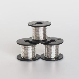 Könnte beinhalten: Drei schwarze Kunststoffspulen, die in einer Pyramidenform gestapelt sind und jeweils mit einem durchgehenden, dünnen, glänzend silberfarbenen Metalldraht umwickelt sind. Die Spulen verfügen über kreisförmige Endkappen und einen Zentralkern.