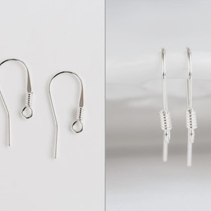 Pode incluir: Um par de ganchos para brincos de metal prateado com um design de fio curvo, um pequeno detalhe de mola em espiral e um laço circular na base para prender componentes de joalharia. Os ganchos são apresentados de frente e de perfil.